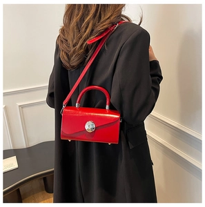 Detail view of red patent leather box bag with silver buckle worn with black blazer