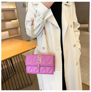 Detail of fuchsia crossbody bag with quilted texture, gold chain and tassel on white coat