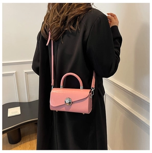 Detail of pink glossy patent leather crossbody bag featuring a large silver round buckle