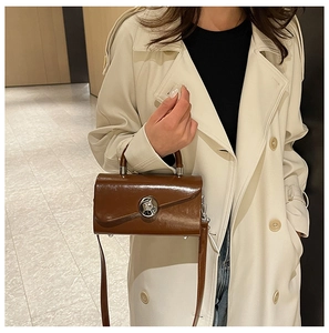 Brown leather crossbody bag with silver buckle worn with a stylish beige trench coat
