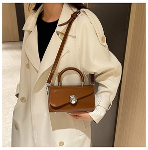 Close-up of brown glossy leather box bag with silver metal buckle on a woman in a trench coat