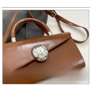 Detail of a dark brown glossy leather bag featuring a large silver round metallic buckle