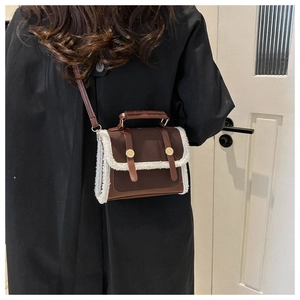 Dettaglio borsa a tracolla in pelle marrone con bordo in peluche su un cappotto nero