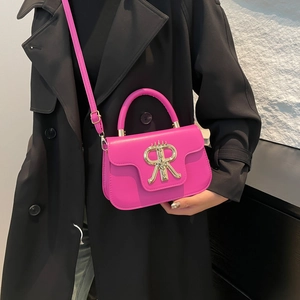 Hot pink mini crossbody bag with gold crown logo worn on a black stylish coat