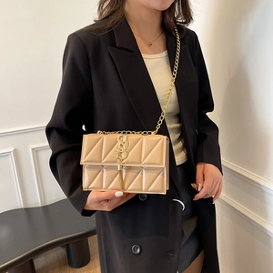 Sac bandoulière beige matelassé avec chaîne dorée et gland sur tenue blazer noir