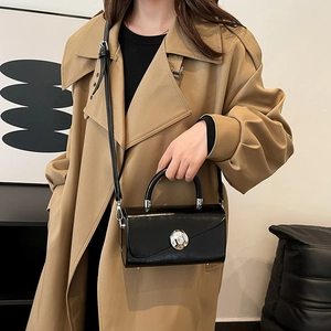 Minimalist black glossy leather box bag with silver buckle worn with a khaki trench coat