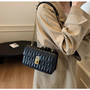 Detail of black quilted matelassé shoulder bag with gold metal chain and push-lock