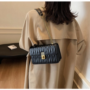 Close-up of black quilted leather shoulder bag featuring a gold twist lock and chain strap