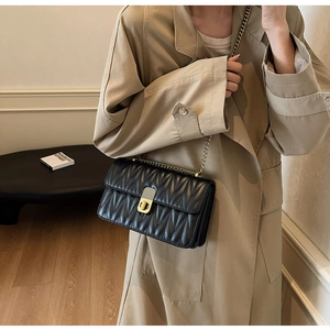 Close-up of black quilted chain bag styled with a beige trench coat for a chic look