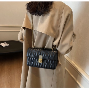 Close-up of black quilted shoulder bag with gold chain strap worn over a beige coat