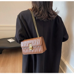 Brown quilted chain bag with V-shaped stitching and gold lock shown on model