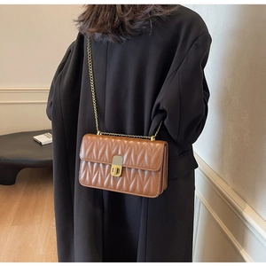 Detail view of brown quilted crossbody bag with gold chain strap on a black coat