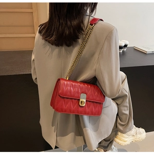 Detail of red quilted faux leather handbag with gold metal clasp and chain shoulder strap
