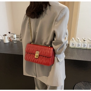 Detail of red quilted shoulder bag with gold chain strap and turn-lock closure on model