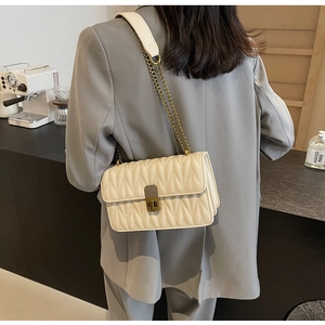 Detail of quilted diamond pattern and gold chain strap on cream shoulder bag