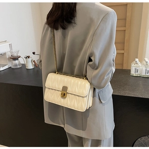 Close-up of quilted cream crossbody bag with gold chain strap and vintage metal lock