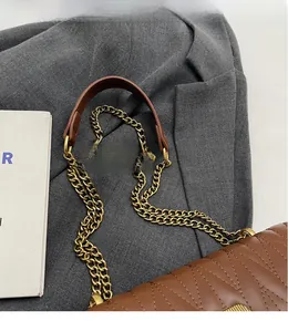 Detail of golden chain strap and brown leather shoulder guard with V-quilt pattern