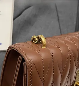Detail of brown quilted leather bag with V-shaped stitching and gold chain hardware