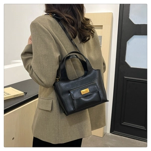Détail du sac seau en cuir noir avec ferrures dorées porté sur un blazer kaki