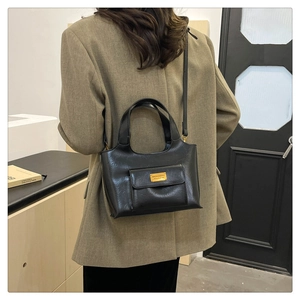 Détail du sac seau en cuir noir avec plaque en métal doré et bandoulière réglable