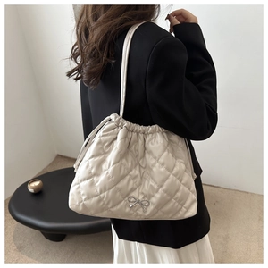 Detail of a quilted ivory bucket bag with a silver bow ornament on a model