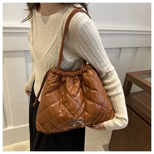 Close-up of brown quilted bucket bag with drawstring and silver bow detail