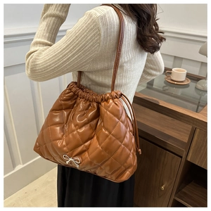 Detail of a brown quilted bucket bag with a silver metal bow buckle and drawstring closure