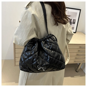 Detailed view of black quilted tote bag with silver bow accent on smooth PU leather