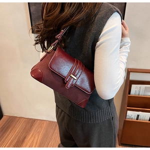 Detail of burgundy leather shoulder bag with gold buckle and mixed textures on a model