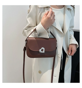 Brown leather crossbody bag with silver heart lock shown on a white trench coat