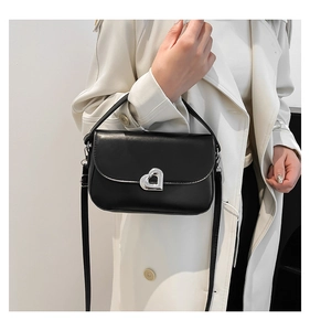 Detail of black faux leather bag featuring a silver heart-shaped clasp and adjustable strap