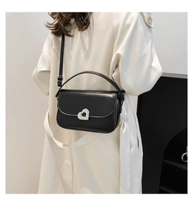 Model wearing a black handbag with silver heart lock and long beige coat in a studio