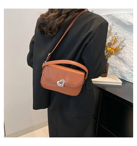 Detail shot of a brown saddle bag featuring a silver heart-shaped metal twist lock closure