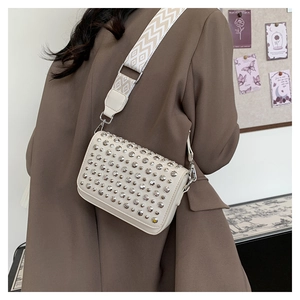 Detail of a beige crossbody bag with silver studs and a wide geometric woven strap