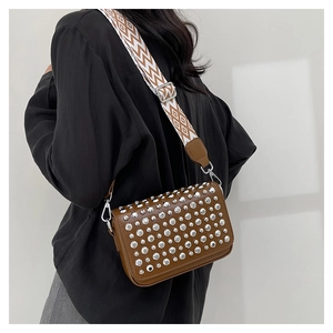 Detail of brown leather rivet square bag featuring a wide geometric patterned strap