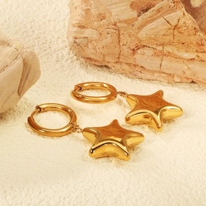 Créoles minimalistes en or 18 carats avec pendentif étoile sur fond de sable naturel