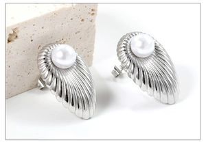 Detail view of scallop shell pearl earrings in silver stainless steel with natural stone backdrop
