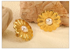 Macro view of gold floral earrings with pearl center on natural stone backdrop