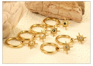 Detailed view of three gold starburst earrings with pearls and green gems on stone
