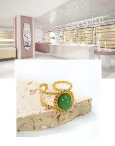 Détail d'une bague dorée avec pierre verte ronde et anneau à double rangée de perles