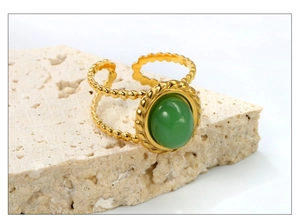 Détail d'une bague bohème dorée avec pierre verte ovale sur fond de texture pierre