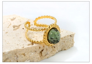 Détail macro d'une bague dorée vintage avec pierre ovale verte et anneau perlé ajustable