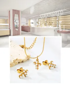 Détail de boucles d'oreilles croix dorées et collier sertis de perles blanches