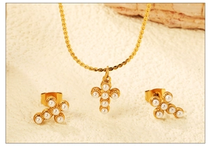 Détail du collier croix dorée et boucles d'oreilles perles sur fond crème minimaliste