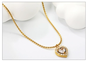 Close-up of gold heart pendant necklace featuring sparkling zircon crystals on white decor