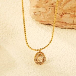 Golden teardrop pendant necklace with clear zircon stone on white textured background