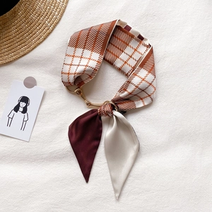 Détail d'un foulard étroit à carreaux avec boucle dorée sur un fond texturé blanc