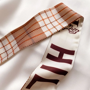 Détail d'un foulard étroit en soie avec motif à carreaux marron et imprimé lettre HI