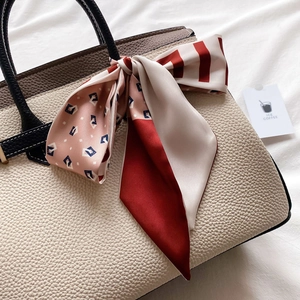 Détail d'un foulard en soie imprimé noué sur l'anse d'un sac à main en cuir beige clair