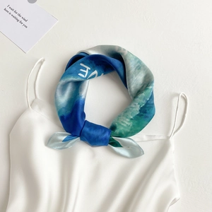 Close-up of silk square scarf in blue gradient wave pattern knotted on white top